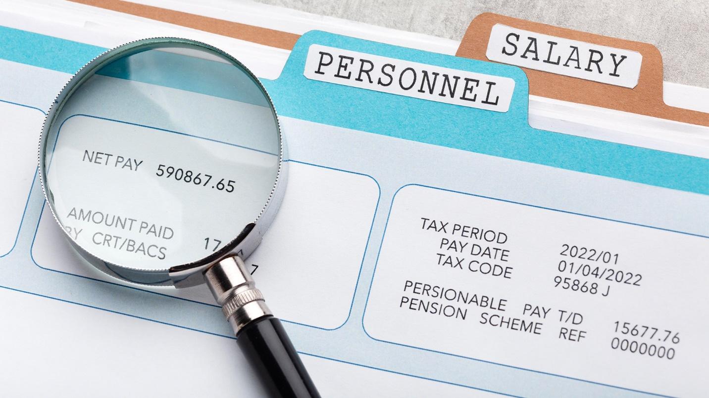 A magnifying glass rests on personnel and salary file folders and a chart showing a net pay amount in a section about salaries for the owners of export services companies. 