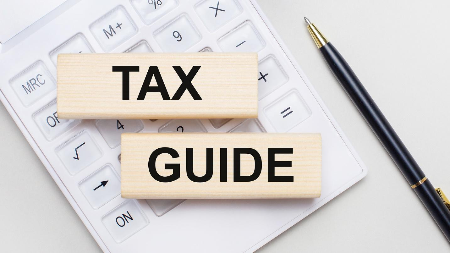 Wooden blocks with the words “Tax Guide” inscribed on them, on top of a calculator and beside a pen.