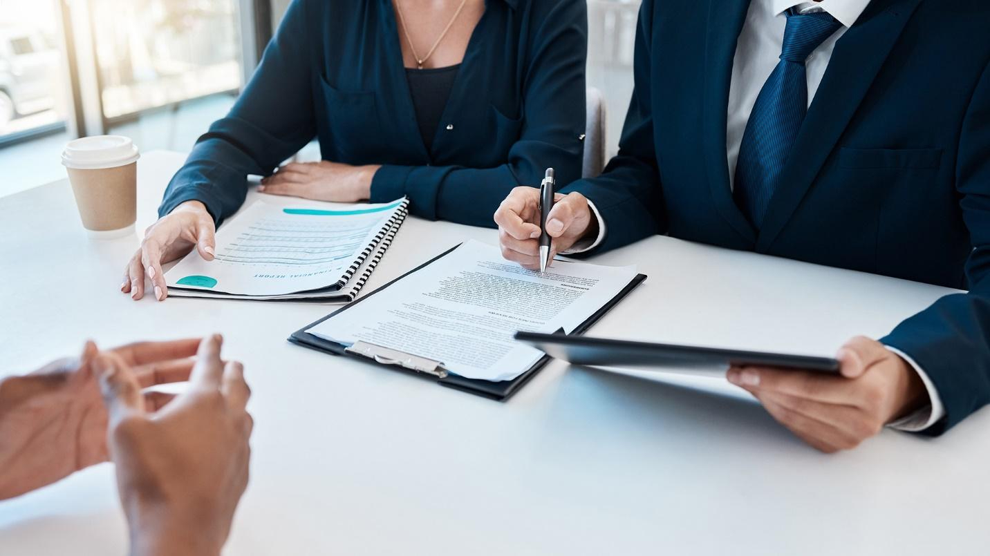 Three people sitting at a white table with documents and a cup of coffee.