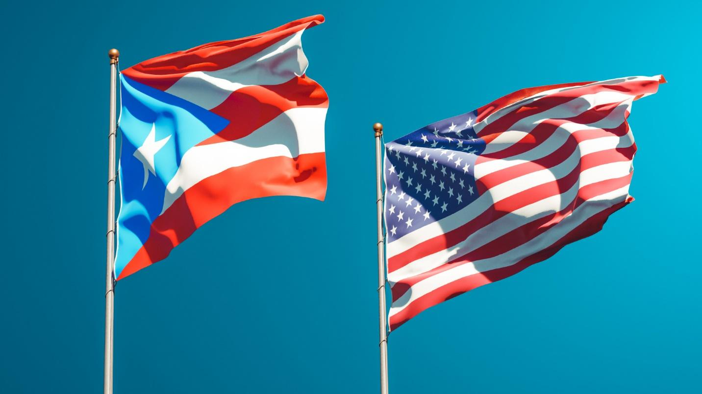 Flag of Puerto Rico flying next to a flag of the United States against a blue background.