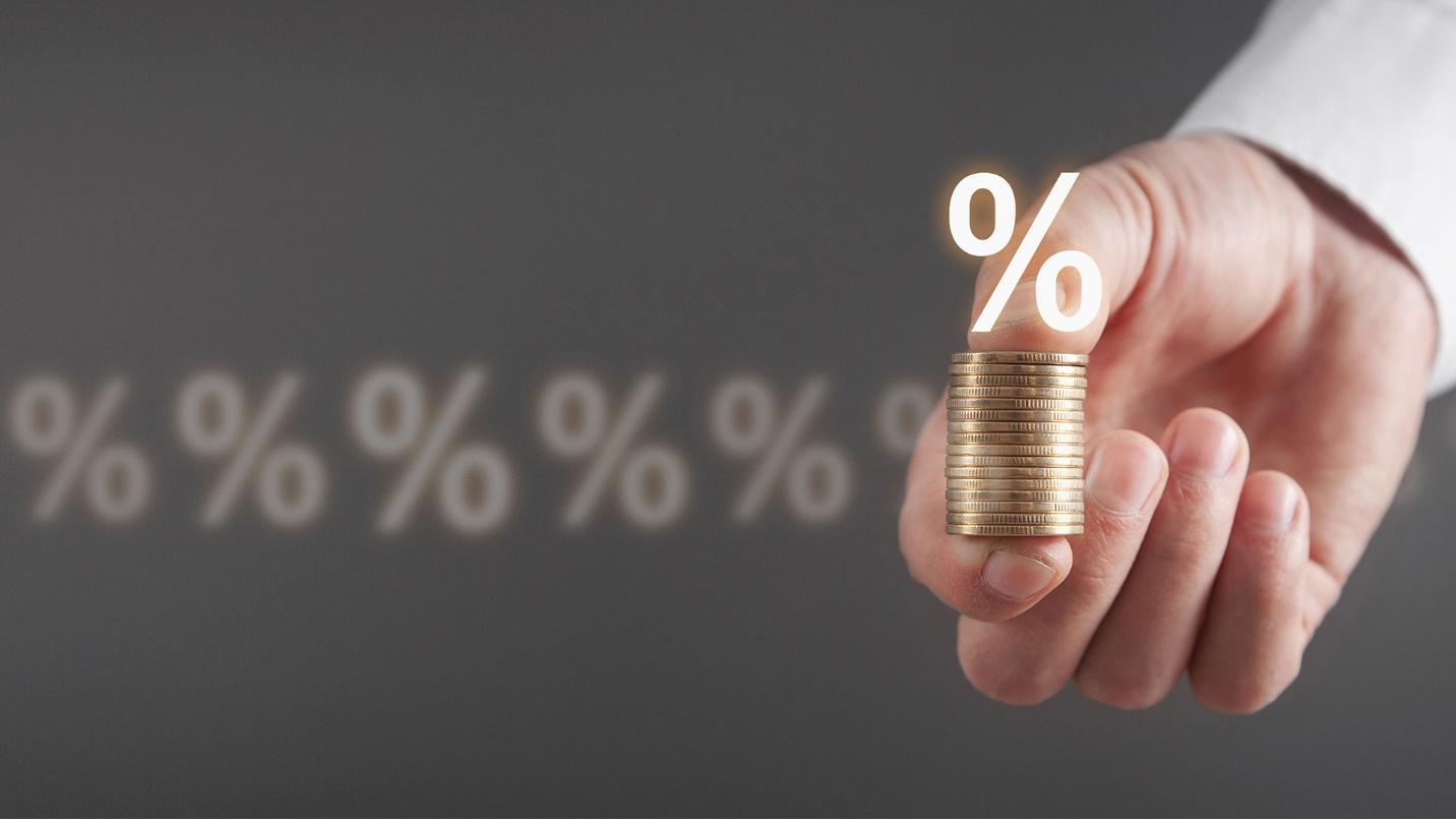 Hand holding a stack of coins with a string of percentage signs in the background.