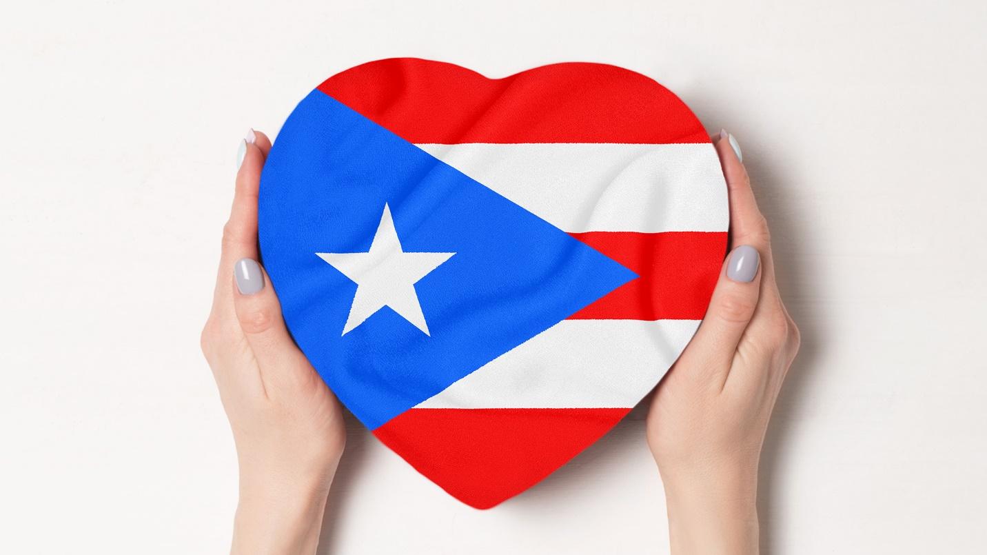 Hands clasp a heart-shaped box decorated with the flag of Puerto Rico in a section about the benefits of relocating to the island and how to get in touch with PRelocate.
