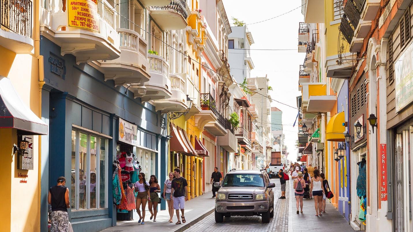 Puerto Ricans walk along sidewalks flanked by stores in a section that describes shopping malls including the largest shopping mall in the Caribbean as well as where to buy international brands and products by local names in Puerto Rico.