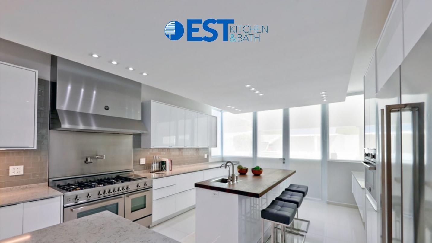 A modern kitchen with white cabinets and stainless steel appliances in a section about EST Kitchen and Bath’s furniture and home appliances.