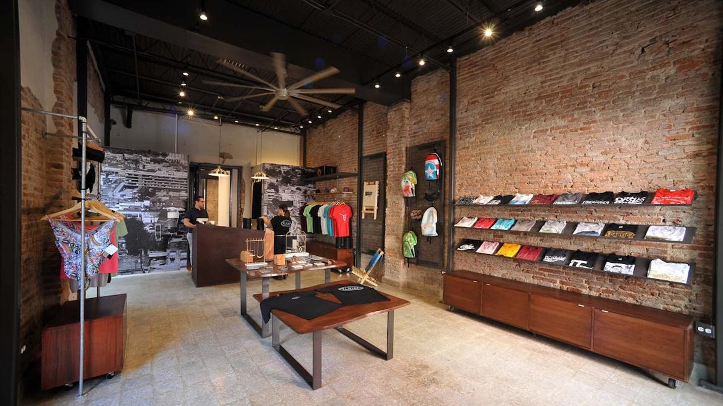 Racks of garments beside brick walls in a section describing the clothing, art, and food at El Nido Puerto Rico.
