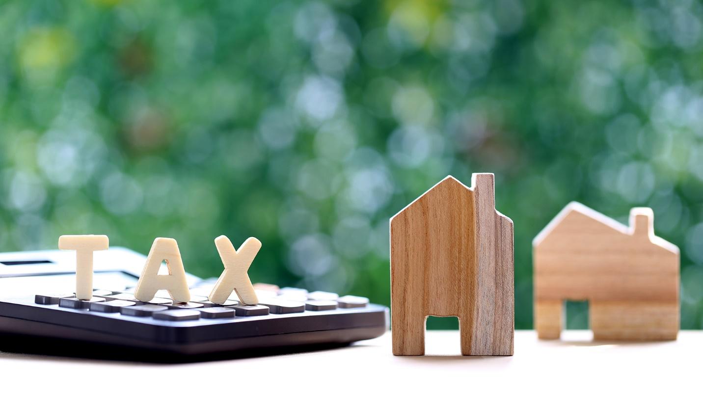 Block letters spell out the word “TAX” on top of a calculator beside two model wooden houses in a section about the requirements of the tax home test.
