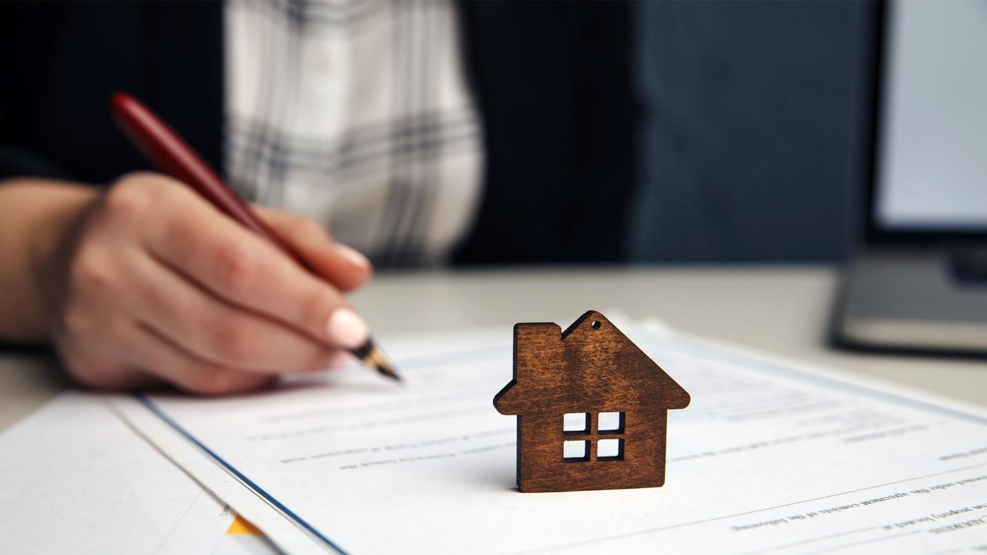 A brown model house rests on papers that a person is filling out in a section that defines the declaration of domicile.