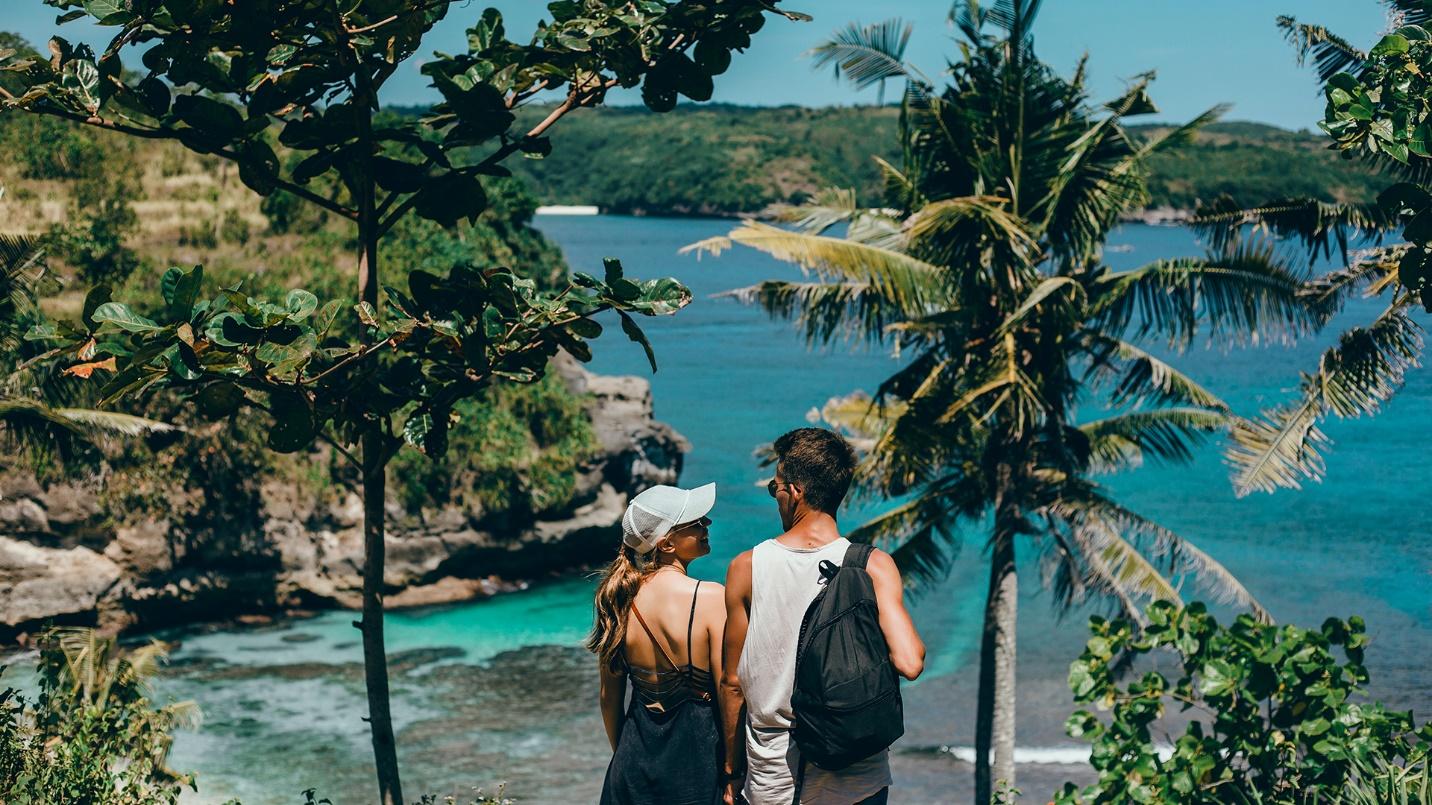 A young man and woman stand on a tree-covered hill overlooking the sea and green landmasses in a section about whether Americans need a passport to travel to Puerto Rico.
