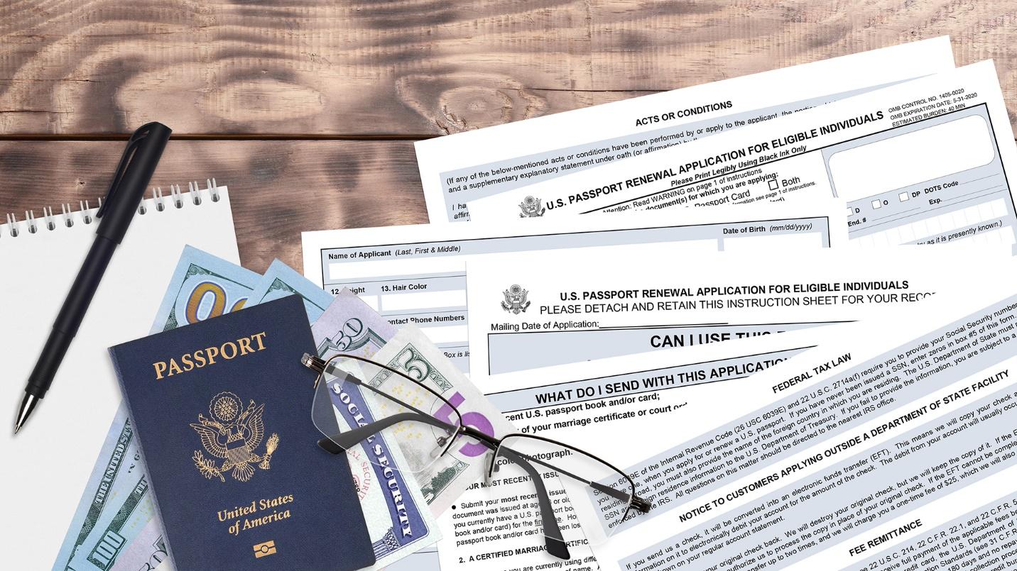 A passport, cash, glasses, and papers rest on a wooden table in a section that explains what an applicant needs to renew a passport.
