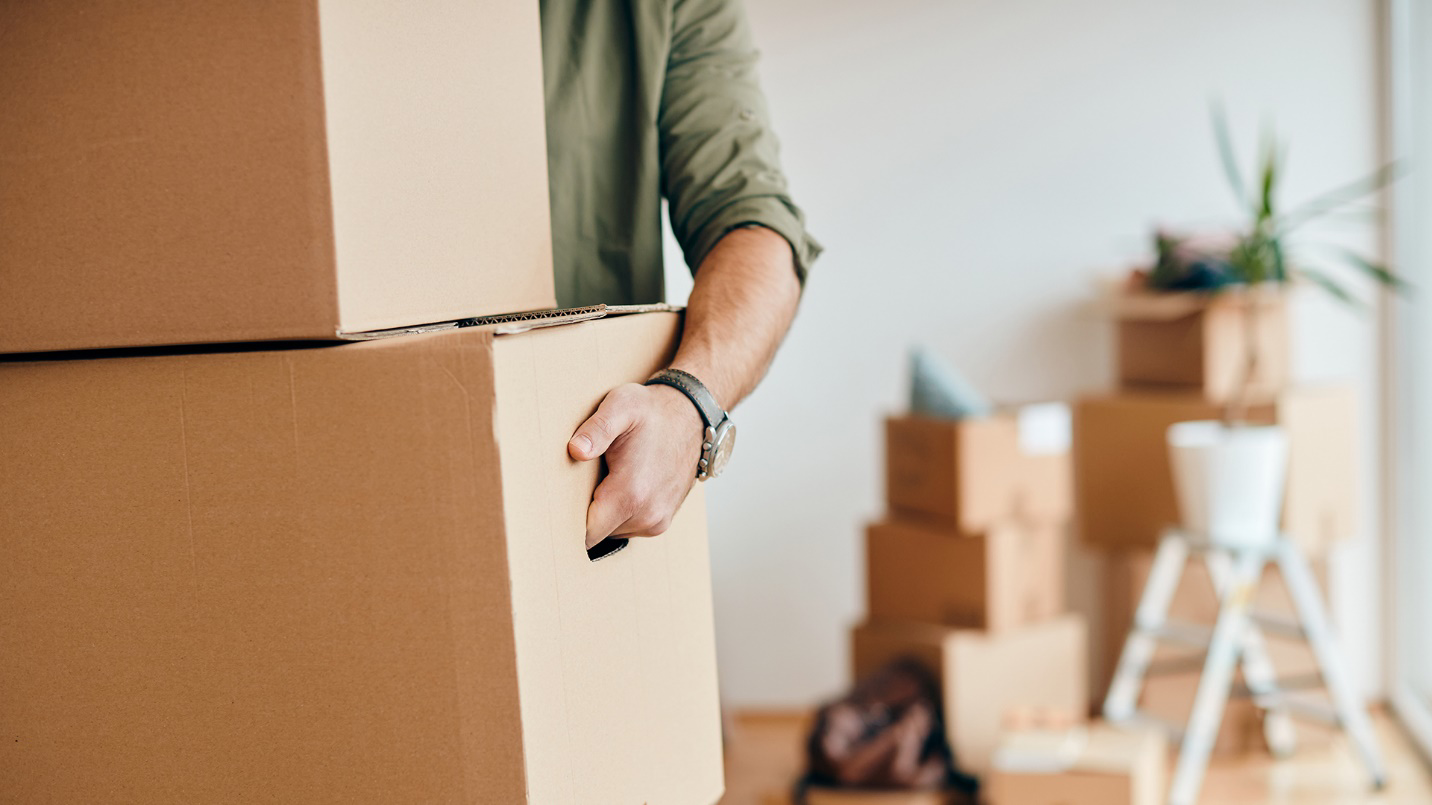 A man carries cardboard boxes out of a room filled with other boxes in a section about the advantages of relocating to Puerto Rico now.
