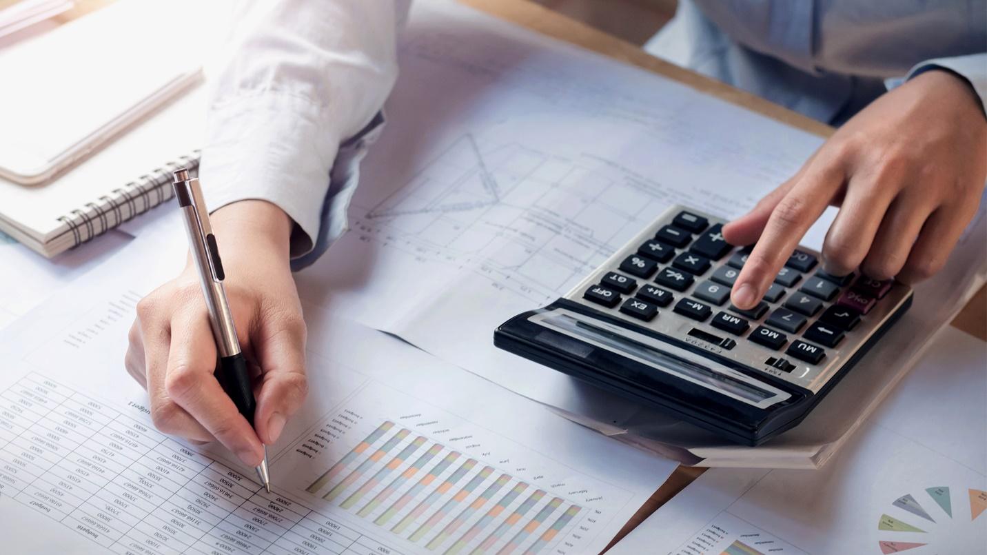 A person writes at a desk that holds paperwork and a calculator in a section that explains how to reduce pre-move capital gains taxes.