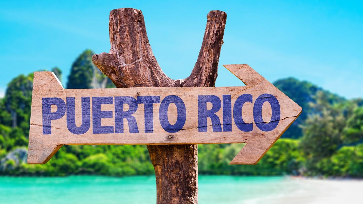A sign that reads “PUERTO RICO” points to the right with a beach and trees in the background in a section about the benefits the island offers to visitors and residents.