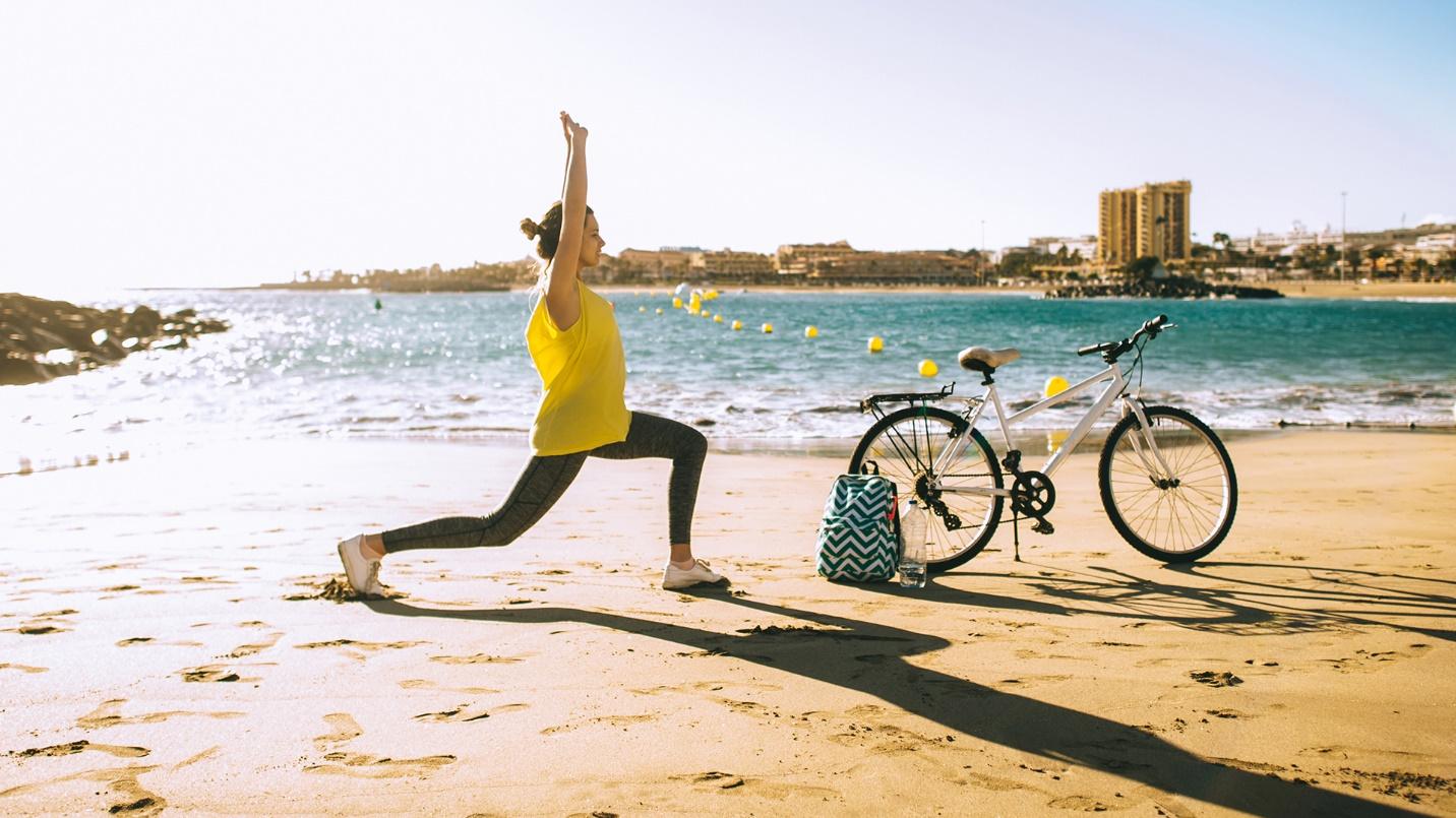 A woman dressed in yellow and black stretches on the beach beside a bicycle and bag in a section describing how to stay fit and active in Puerto Rico.