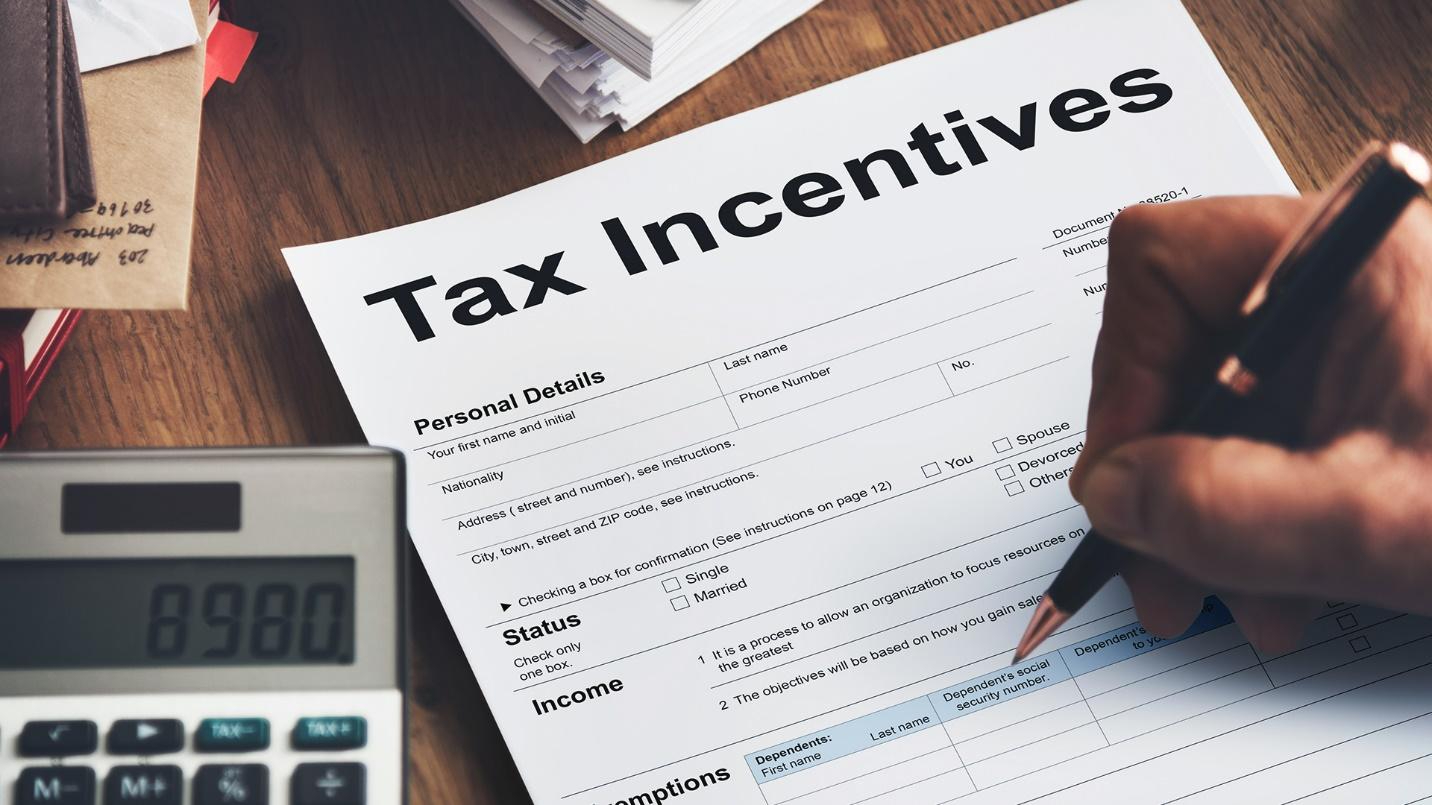 Person holding a pen above a “Tax Incentives” form on a desk with a calculator and papers.
