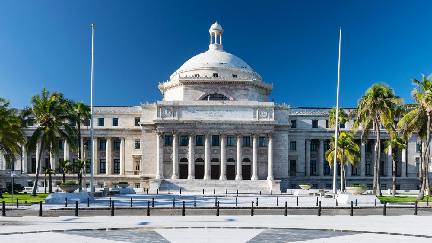 The dome and columns of Puerto Rico’s Capitol Building by palm trees and blue sky in a section about the building’s features.