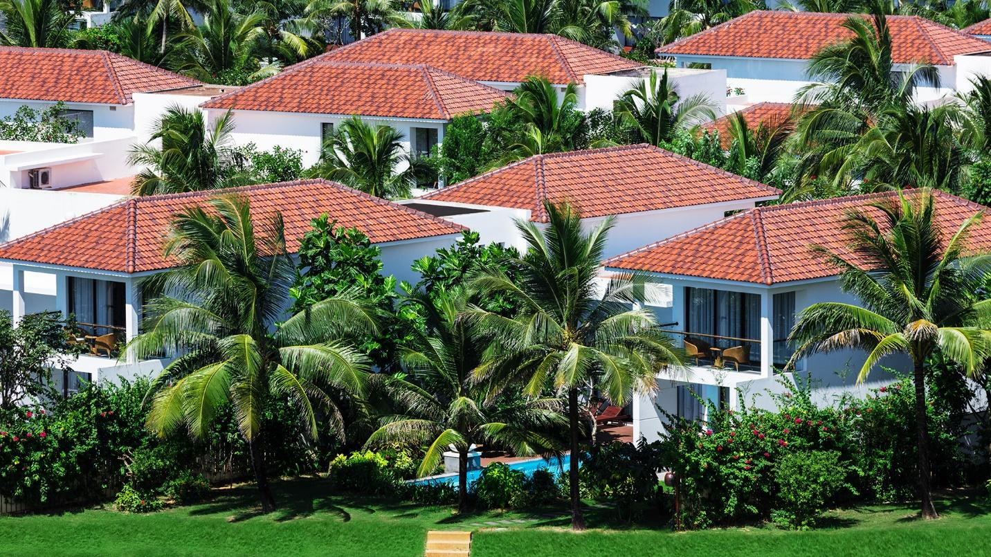 Palm trees, shrubs, and two-story homes with red roof tiles.