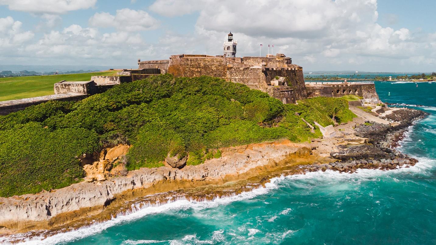 Green hills adjoin the gray walls of El Morro by the coast in a section about the fort’s history and what to see there.