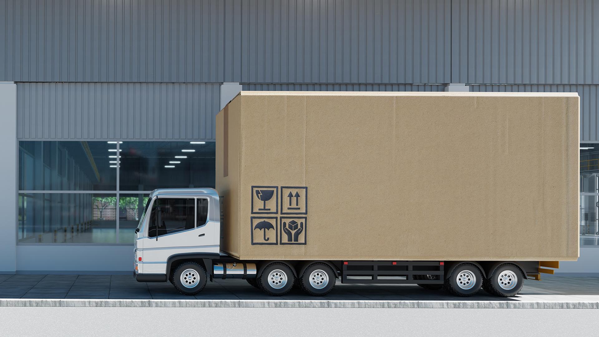 A box truck carrying a giant cardboard box marked with icons (broken glass, up arrows, umbrella, and hands clasping a box) indicating the contents are fragile, should be kept dry, and should be handled with care.