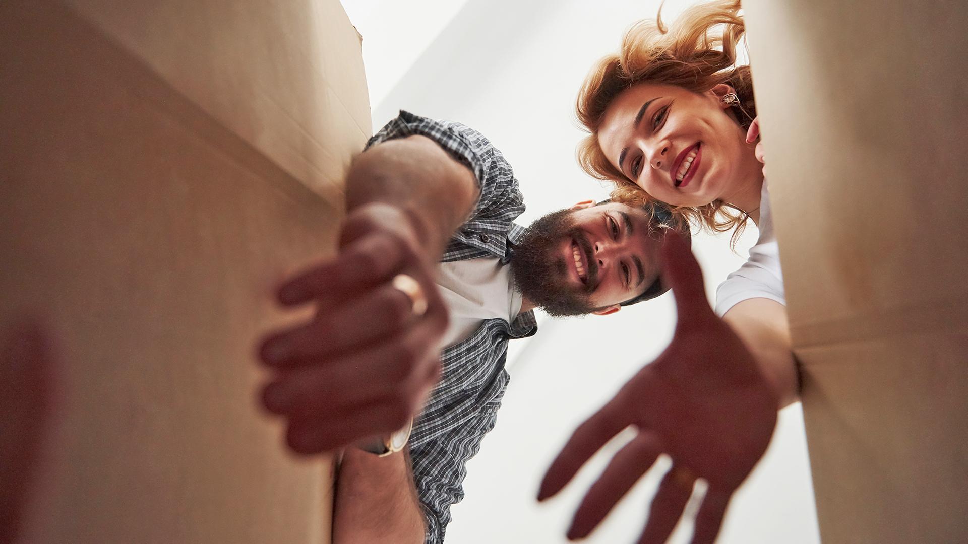 A man and woman smile as they reach into a cardboard box.