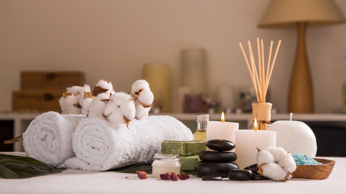 Rolled-up towels, cottonballs, candles, black basalt stones, blue bath salts, and bars of soap.
