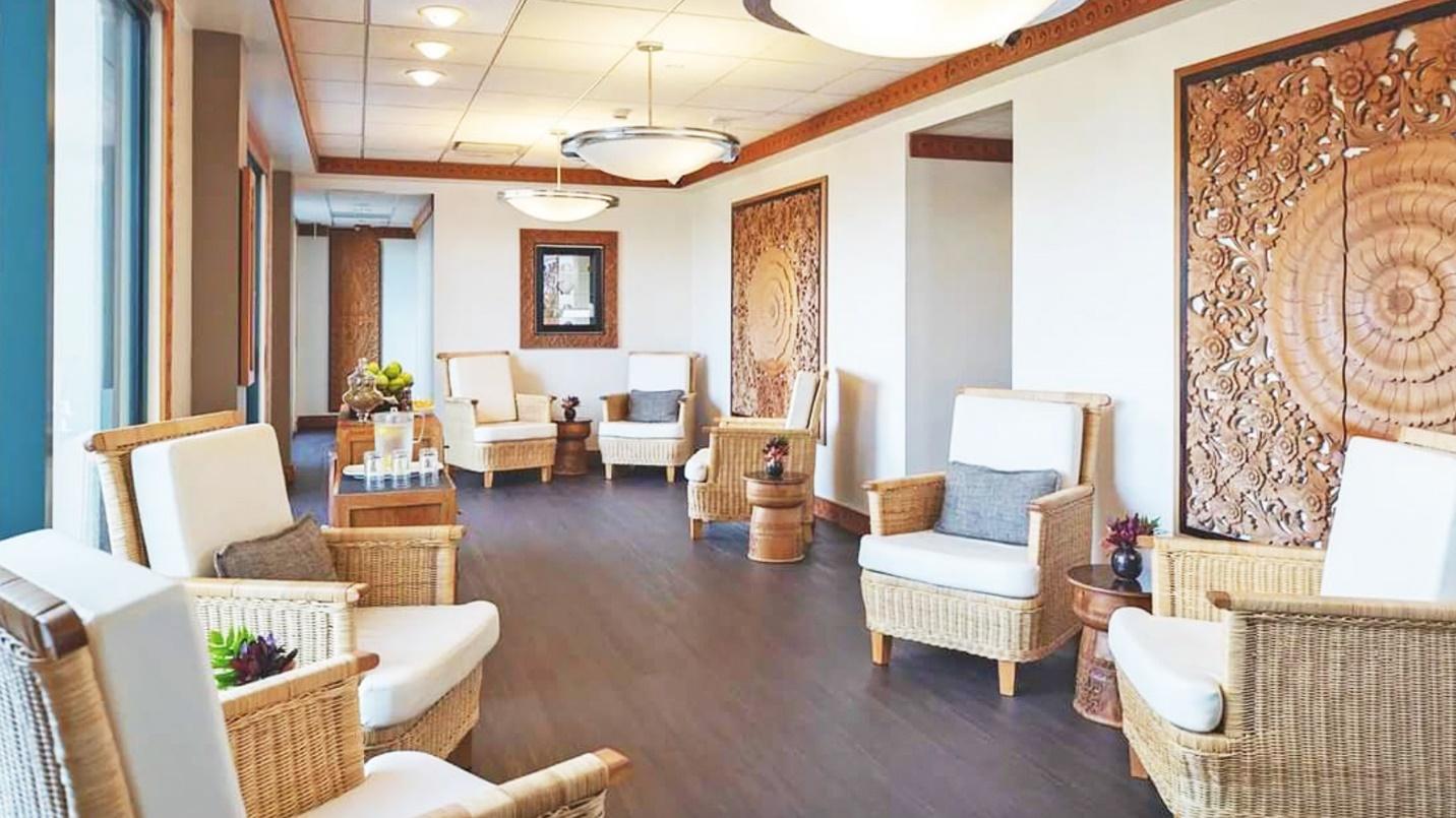 A room with seven white and brown wicker chairs, end tables, white walls, and brown hardwood floors.
