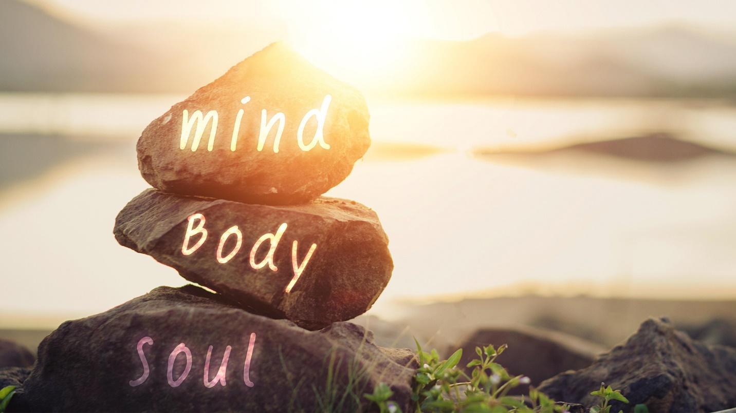 A stack of three stones, each inscribed with the word “mind,” “body,” or “soul,” illuminated by the light of the setting sun.
