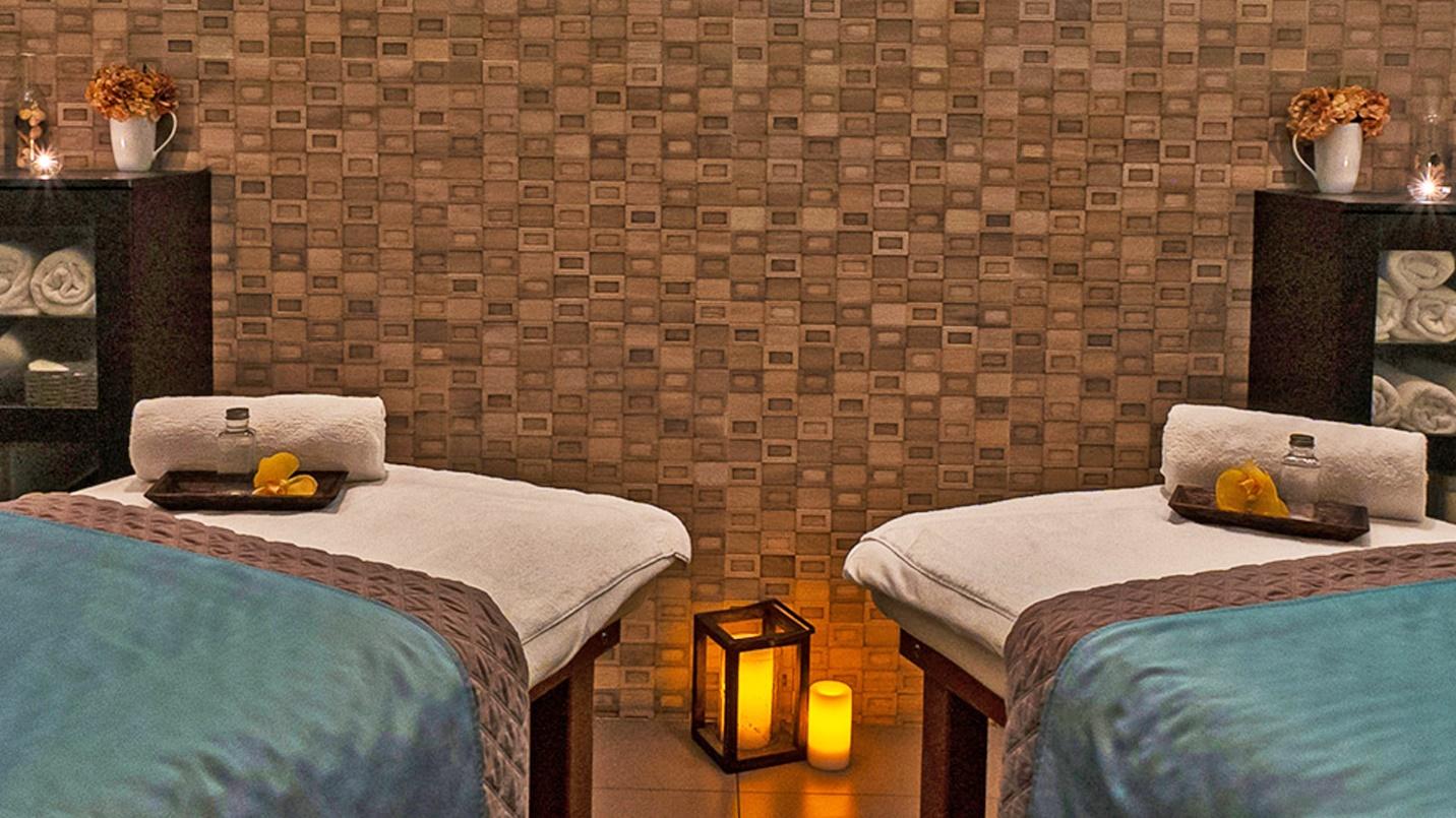 A room with matching massage tables and rolled-up towels, with lit candles on the floor.
