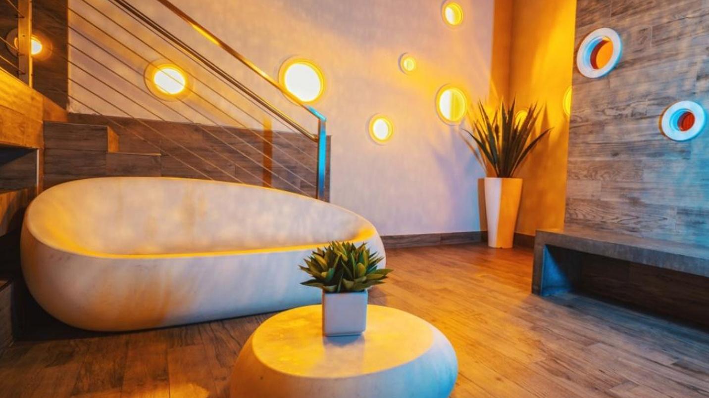 A spa’s lobby with cloud-themed decor, including a rounded couch, table, and circular wall lights, as well as a bench, potted plants, and a staircase.
