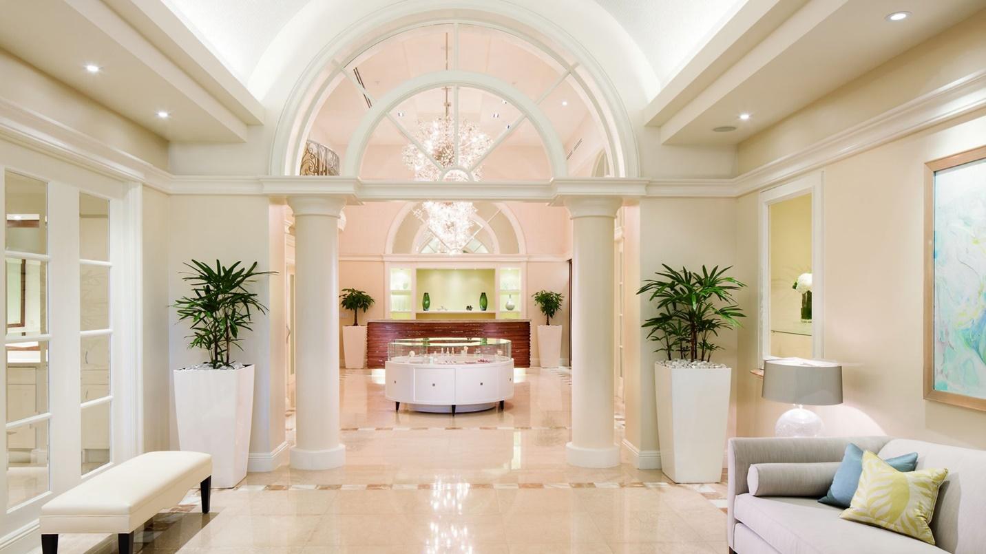 A lobby with white columns, a tile floor, a bench, a couch, potted plants, and recessed lighting.
