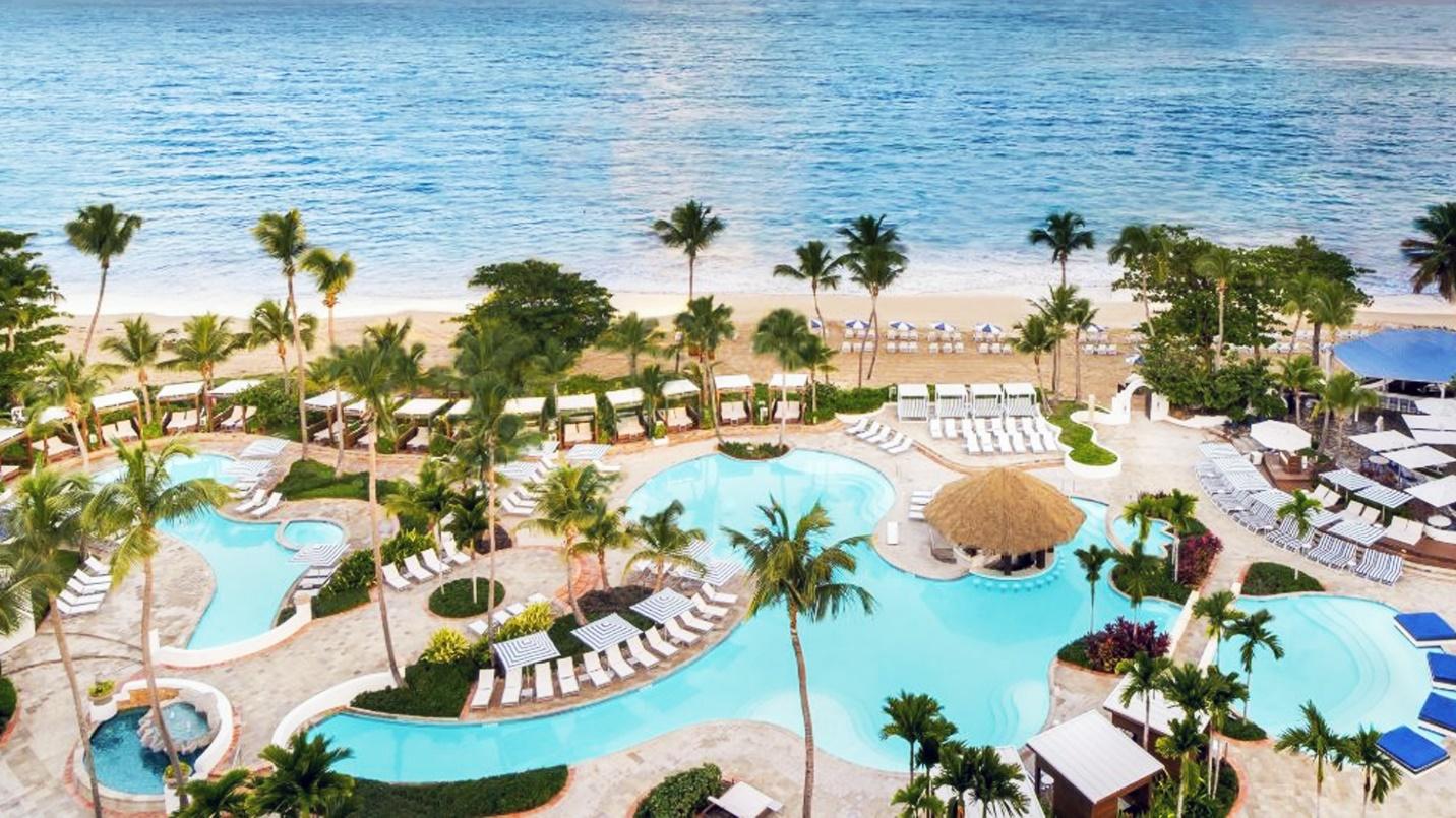 A beachfront resort with pools, chairs, and palm trees.
