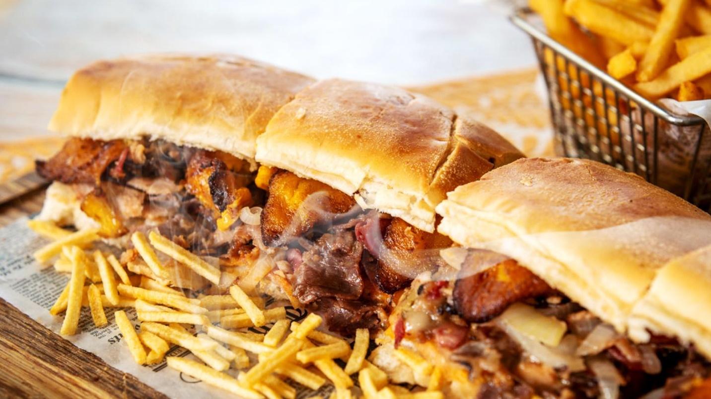 Breakfast treats including sandwiches with plantains and fries rest on newsprint at a table in a section about Pannes restaurant.