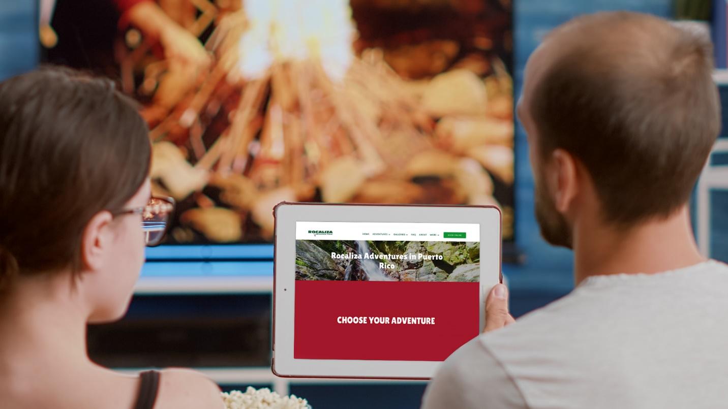 A man and woman look at a computer tablet displaying an ad for Rocaliza Adventure Tours in a section describing the company’s zip line tours.