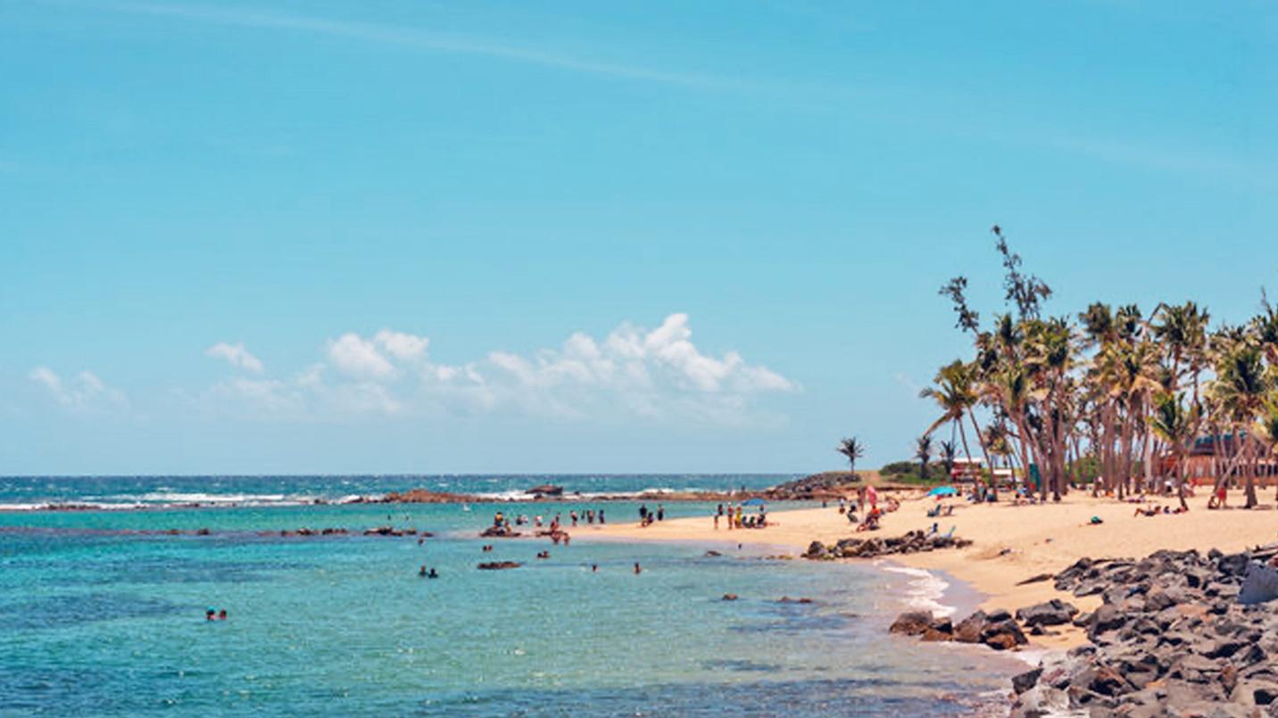 Swimmers and sunbathers at a beach in a section describing Balneario El Escambron.