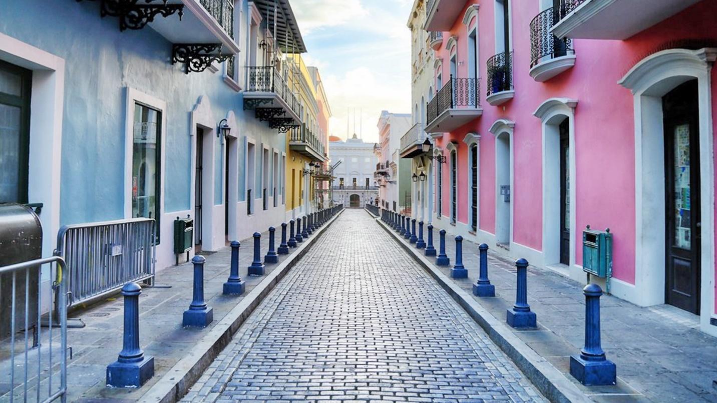 Pastel blue, pink, and yellow buildings flank a cobblestone street in Old San Juan.