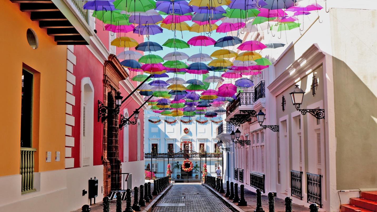 A series of brightly colored umbrellas form a canopy overhead on Umbrella Street in Old San Juan.