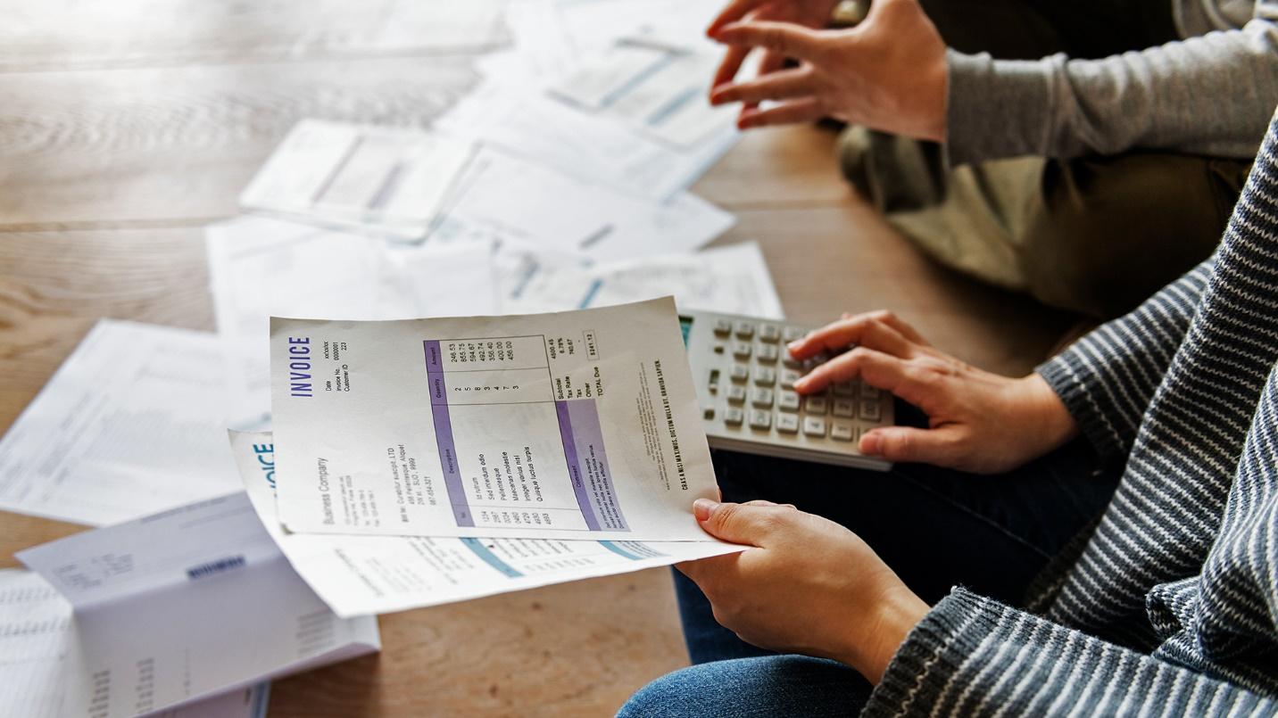 Two people review invoices at a table that holds a calculator and paperwork in a section that explains inflation and how it is calculated. 