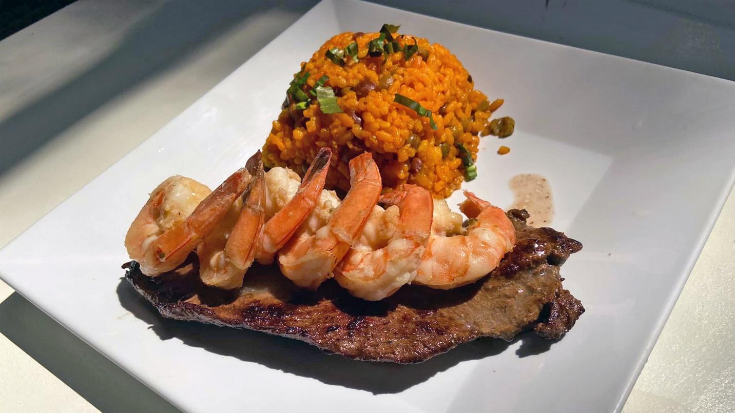 Six shrimp lie on a steak filet next to fried rice and vegetables in a section about Tropical Taste restaurant.