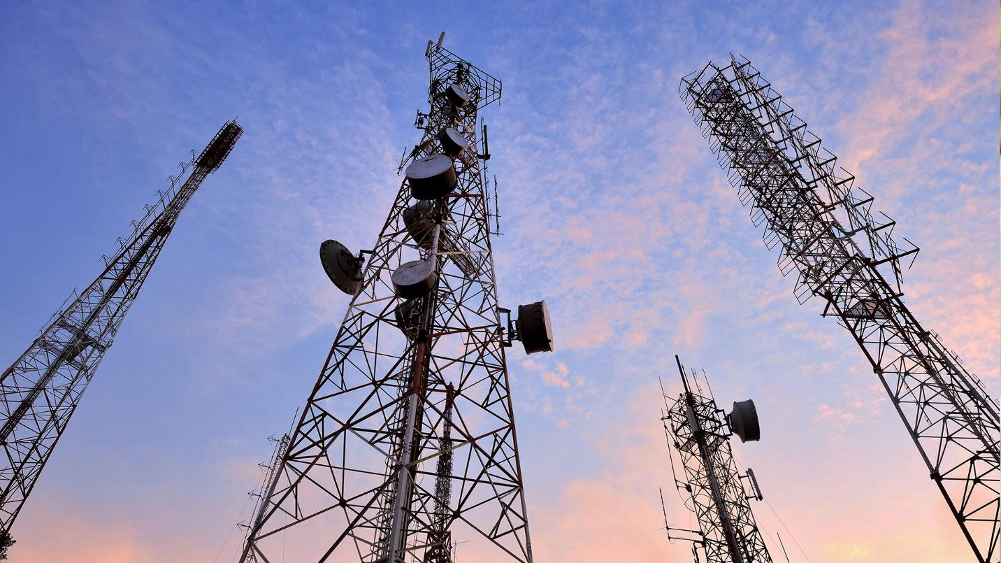 Four cell towers with a blue and pink sky in the background.