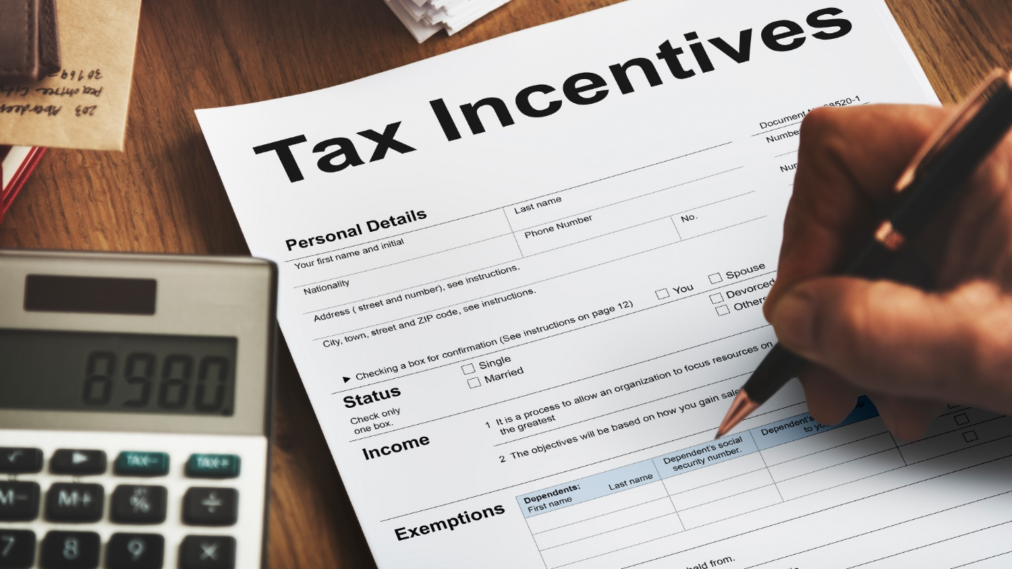 A person holds a pen above a form labeled “Tax Incentives” beside a calculator, letter, and papers.