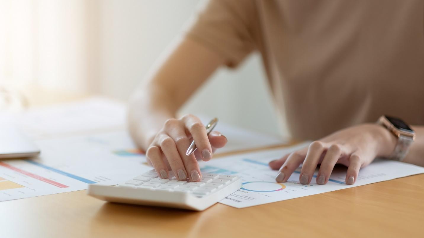 A person sitting at a desk and reviewing numbers on paper and on a calculator while holding a pen.