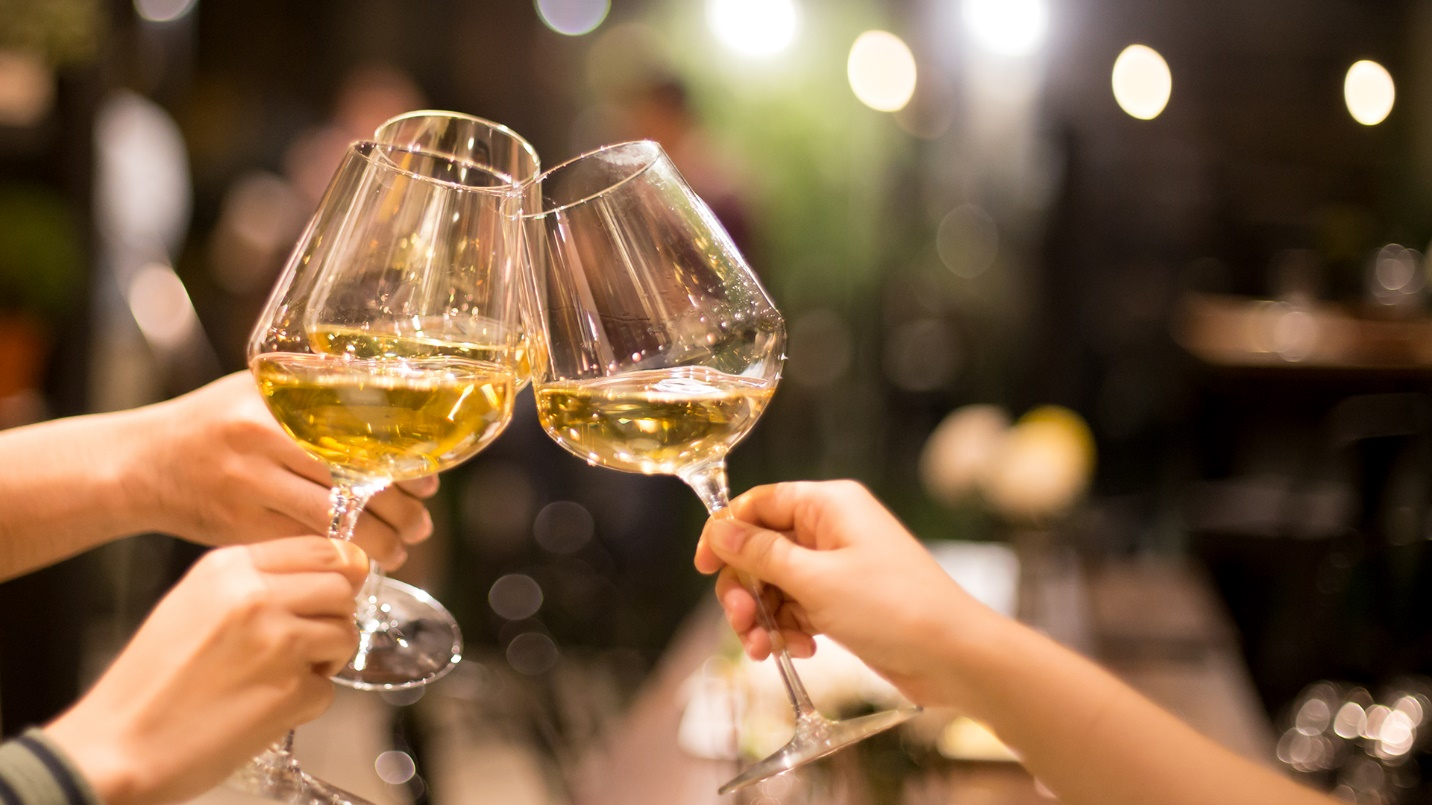 Three people indoors clink their glasses of wine together.