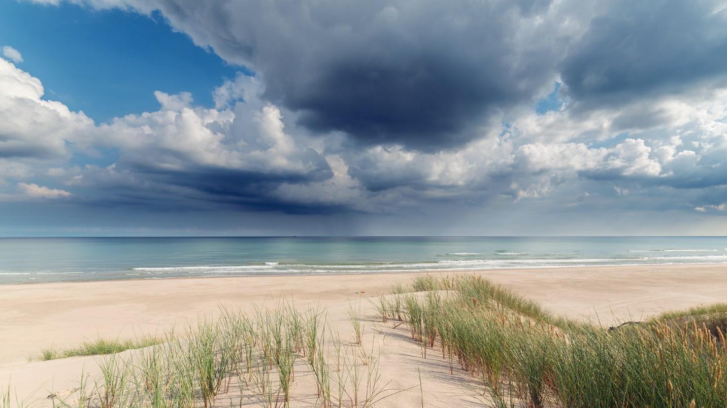 Dark clouds above the sand and water in a section about hurricanes and weather.