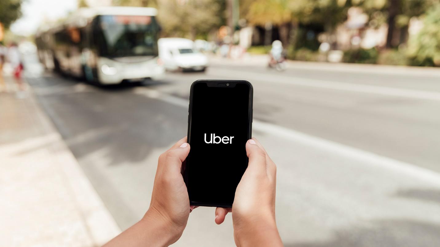 A person standing by the street holds a smartphone that displays the sign for Uber in a section about transport and safety.