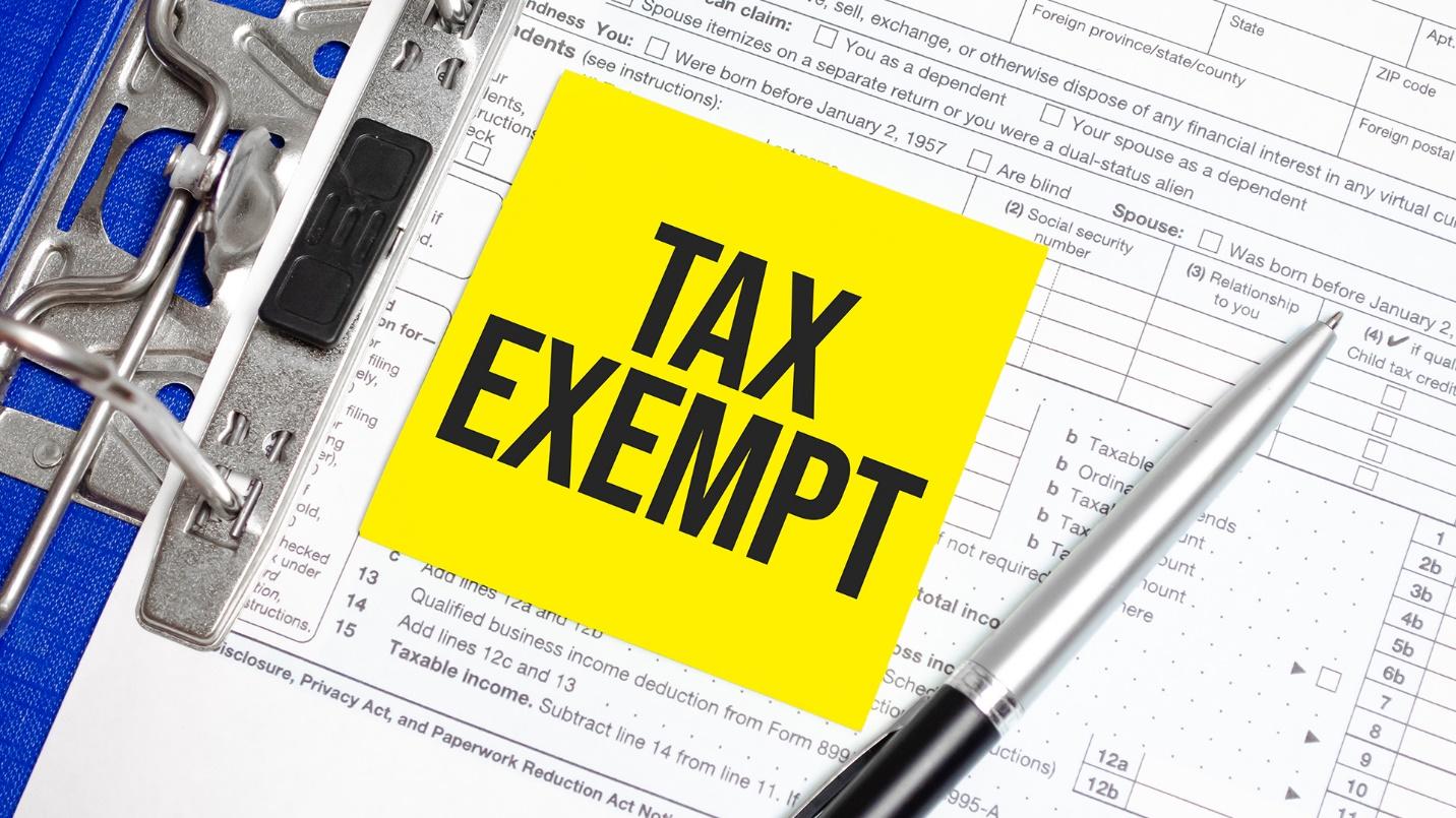 A clipboard holds tax forms and a sticker that reads “TAX EXEMPT” in a section about Puerto Rico’s Act 60 legislation.
