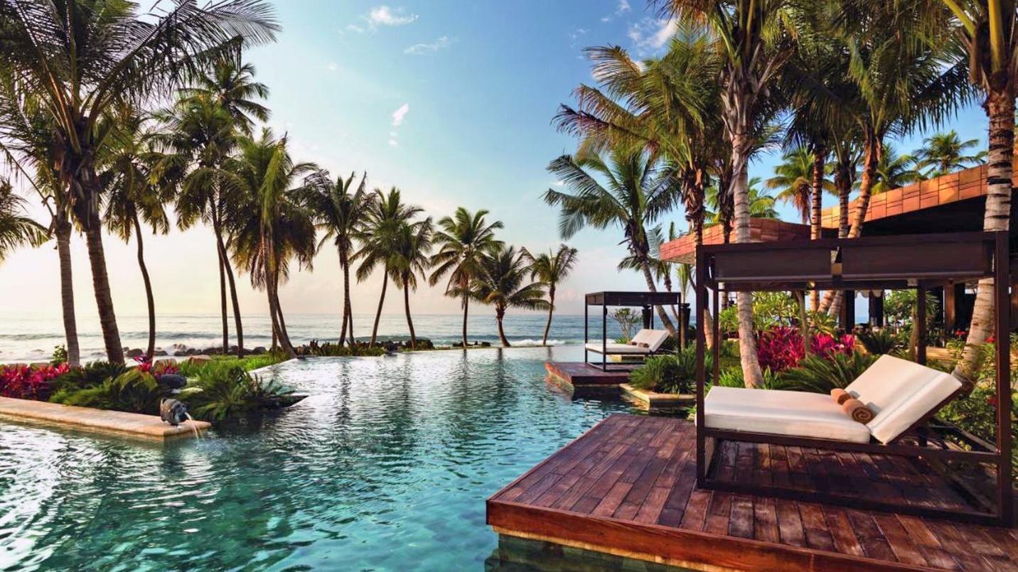 Covered outdoor chaise lounges on decks overlook a lagoon amid palm trees in a section describing the community’s location and history.