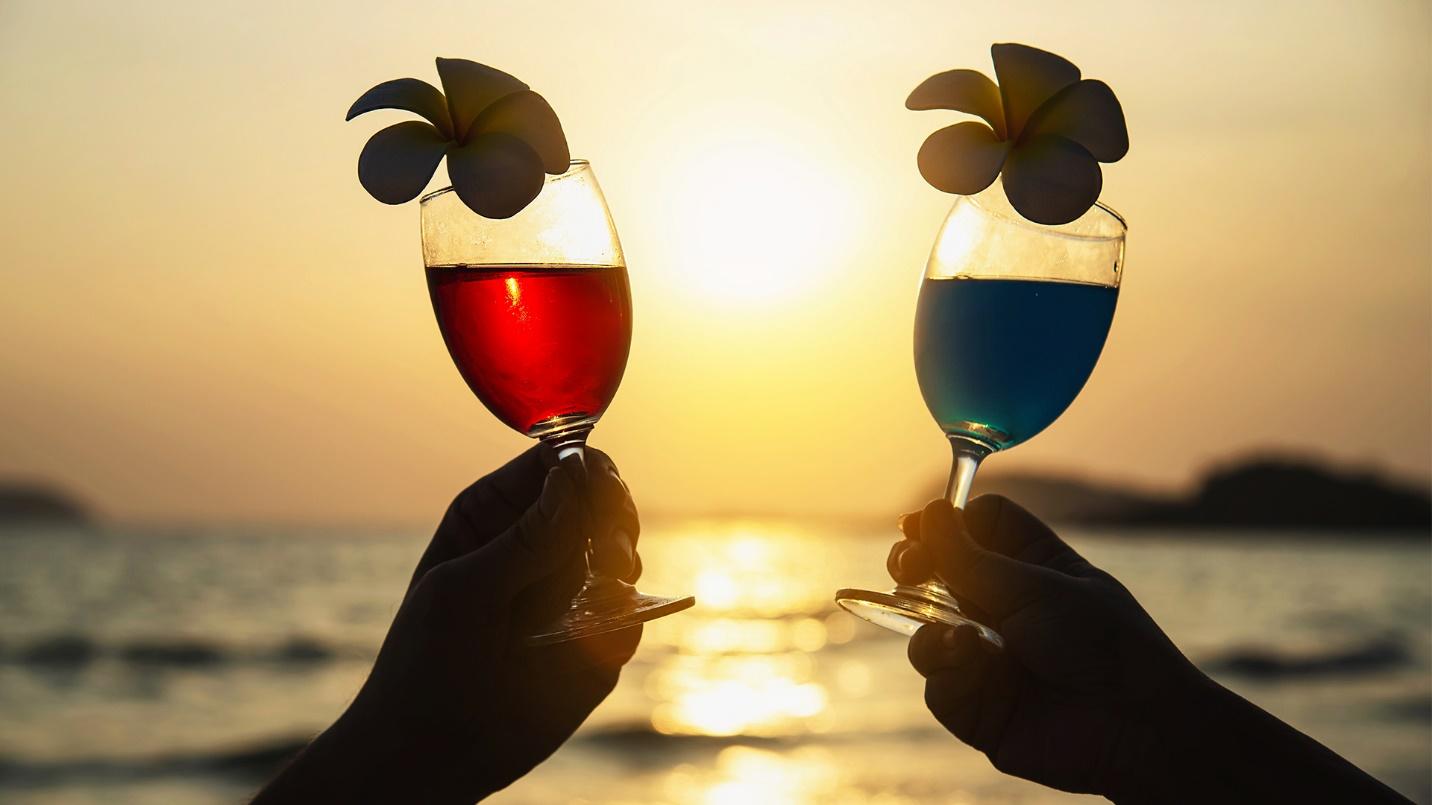 Two hands hold drinks by the sea in the light of the setting sun in a section about nightlife and entertainment.