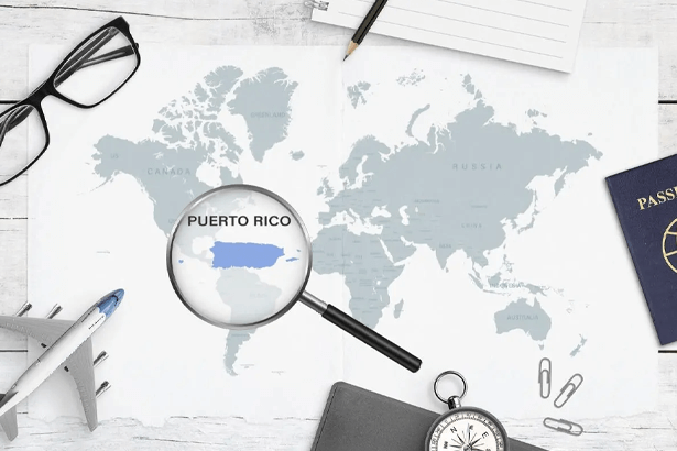 A magnifying glass shows a close-up of Puerto Rico on a world map surrounded by a passport, glasses, and office supplies in a section previewing things to do in Puerto Rico.
