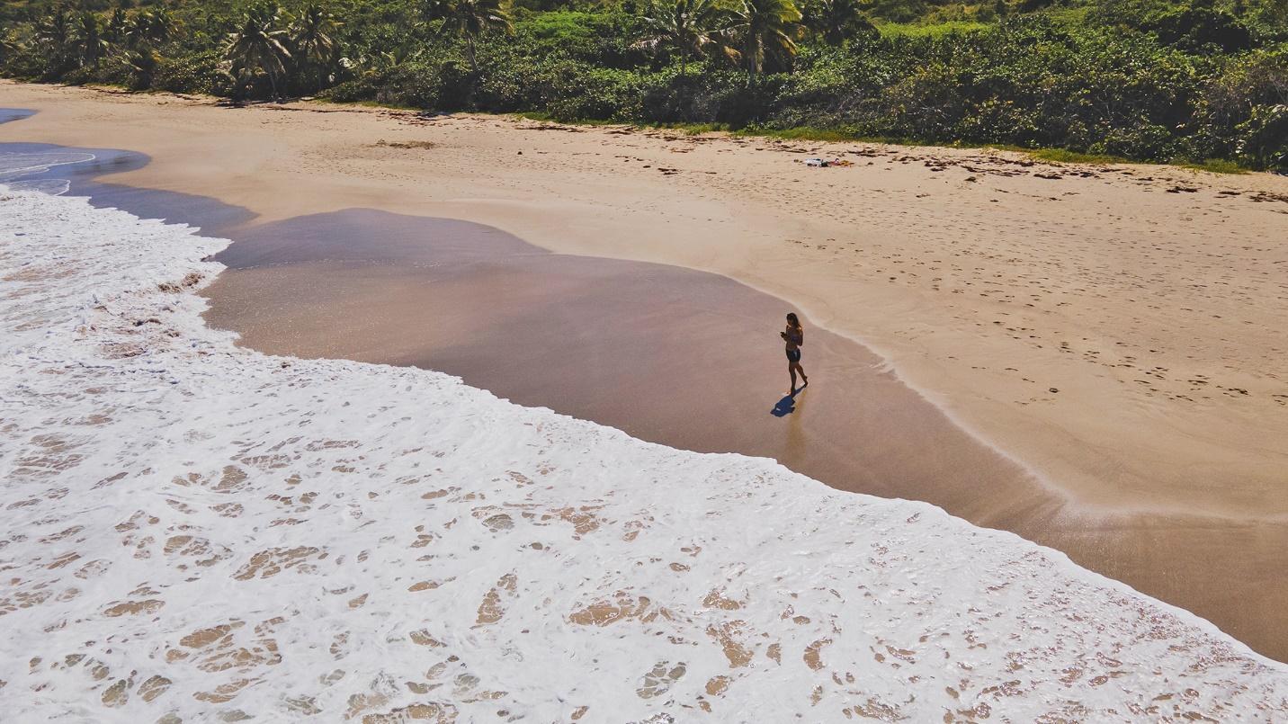 A person walks on the sand by the sea in a section describing Zoni Beach in Puerto Rico.
