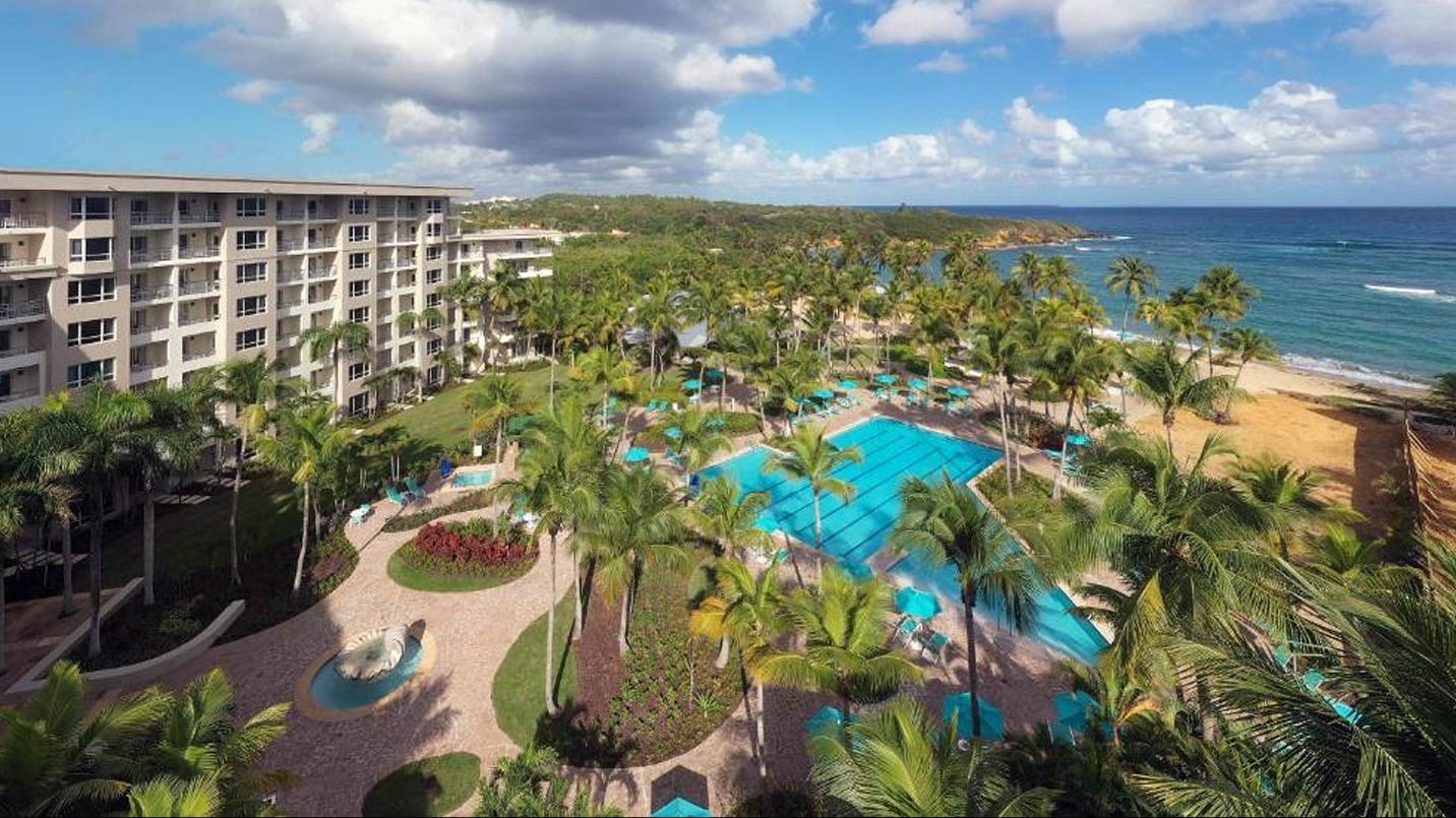 The grounds of Hyatt Residence Club Dorado, including trees, pools, and suites, beside the beach in a section profiling what the hotel has to offer. 