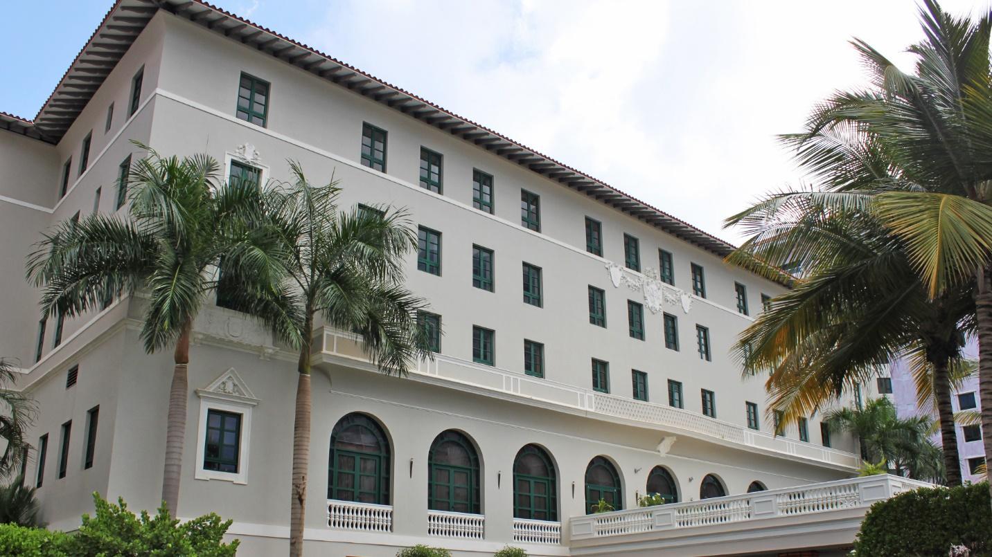 The gray and white façade of Condado Vanderbilt Hotel framed by palm trees in a section describing the hotel’s highlights and prices. 